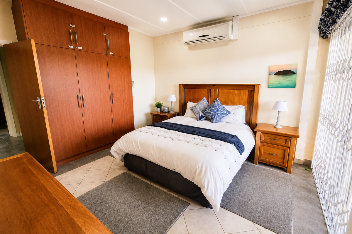 A well-maintained bedroom featuring built-in wooden cupboards, tiled flooring, and a wall-mounted air conditioning unit, with access to a secure patio area.