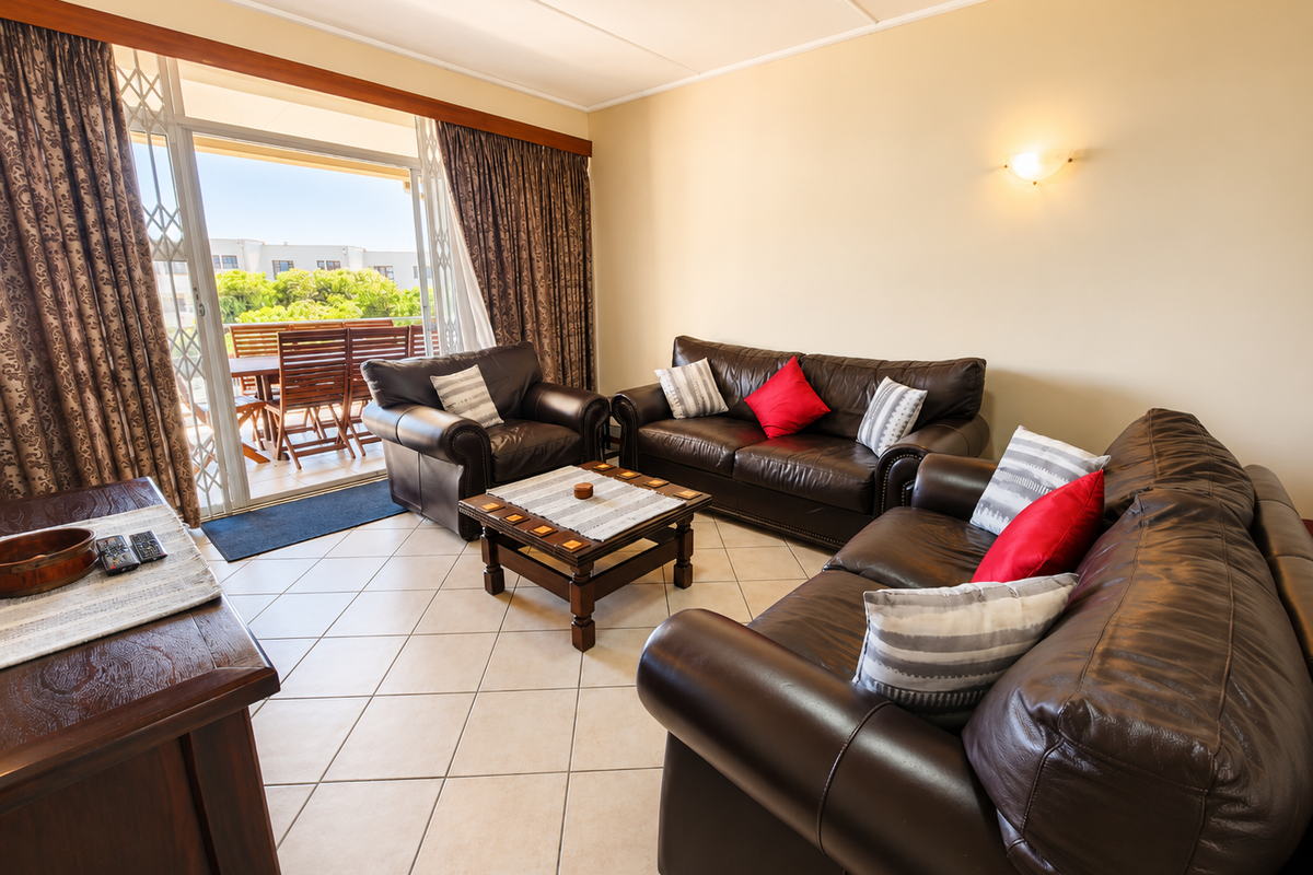 A comfortable living room featuring tiled flooring, wall-mounted lighting, and large sliding glass doors that open onto a private balcony.