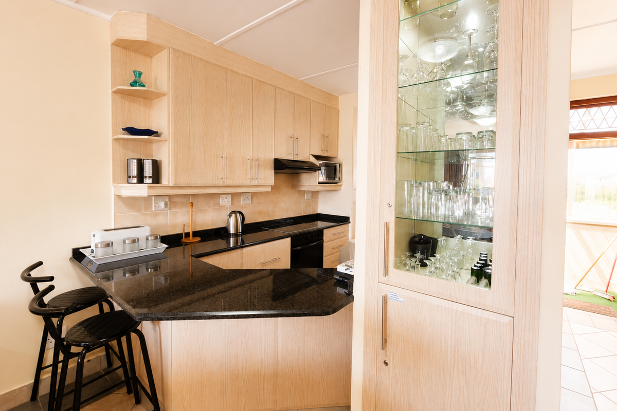 A functional kitchen featuring light wood cabinetry, black granite countertops, a built-in oven, and a glass-fronted display cabinet for glassware.