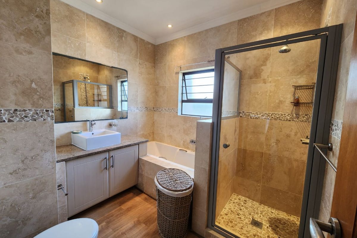 A well-appointed bathroom featuring a separate shower enclosure, a built-in bathtub, a vanity with a vessel sink, and neutral stone-look wall tiling.