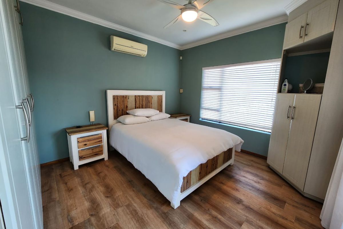 A well-maintained bedroom featuring wood-look flooring, built-in cabinetry, a ceiling fan, and a wall-mounted air conditioning unit.