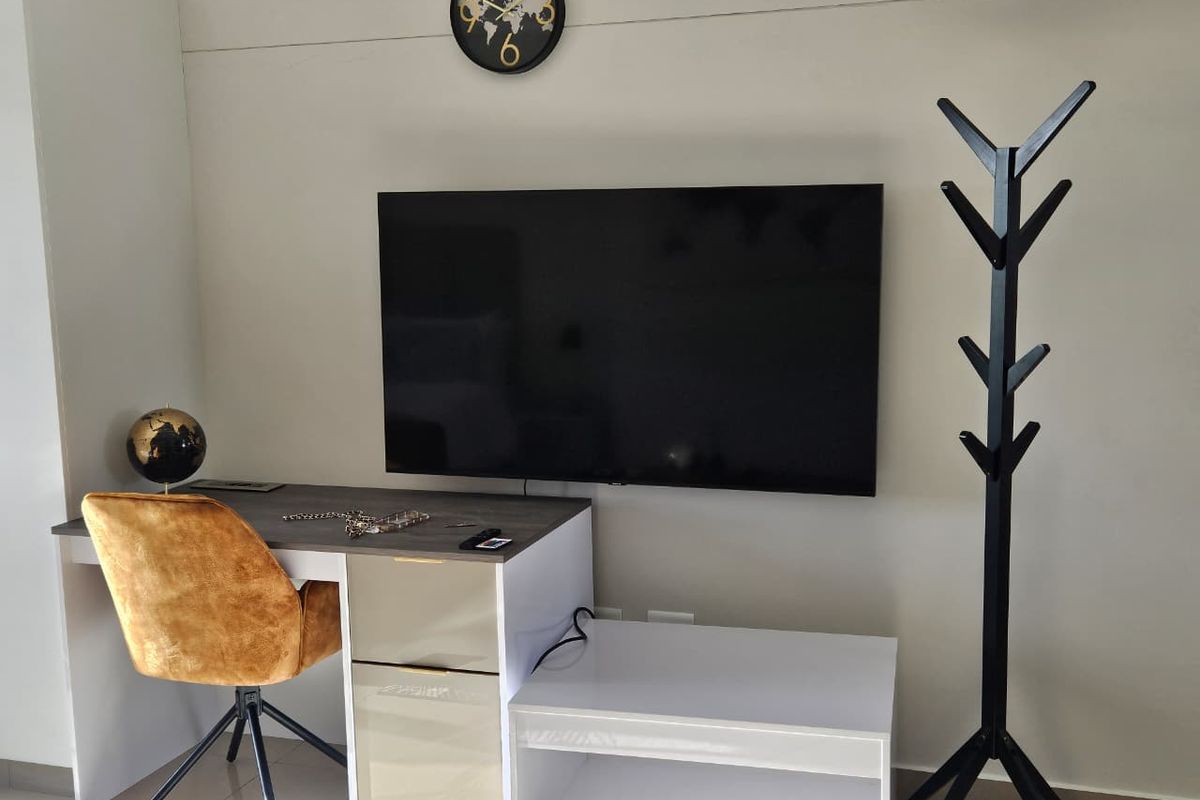 A functional living area featuring a wall-mounted television, integrated desk space, and a split-system air conditioning unit.
