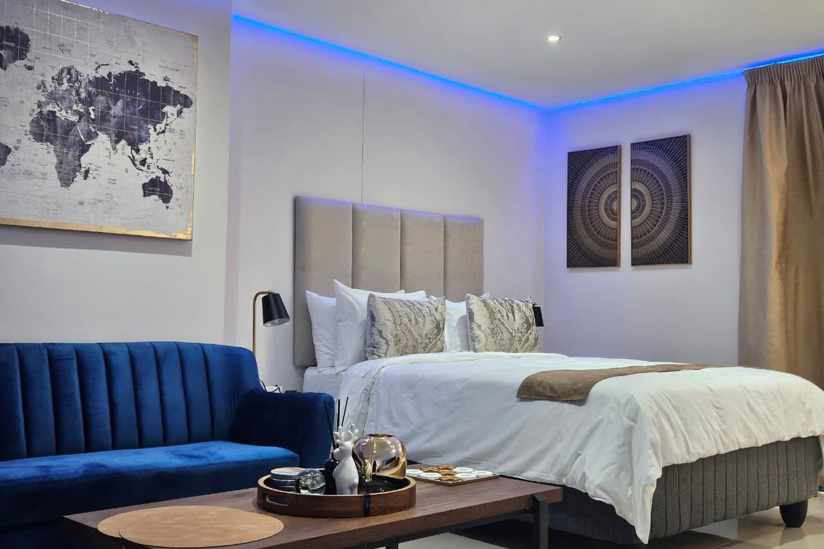 A modern bedroom featuring a built-in upholstered headboard, recessed ceiling lighting with blue LED accents, and tiled flooring.