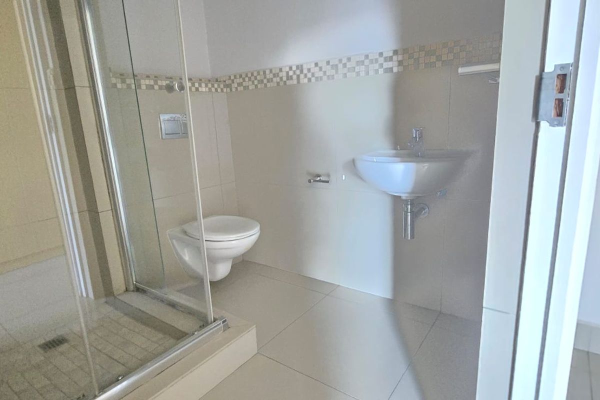 A clean, modern bathroom featuring a glass-enclosed shower, wall-mounted toilet, and a wall-hung basin with neutral tiling.