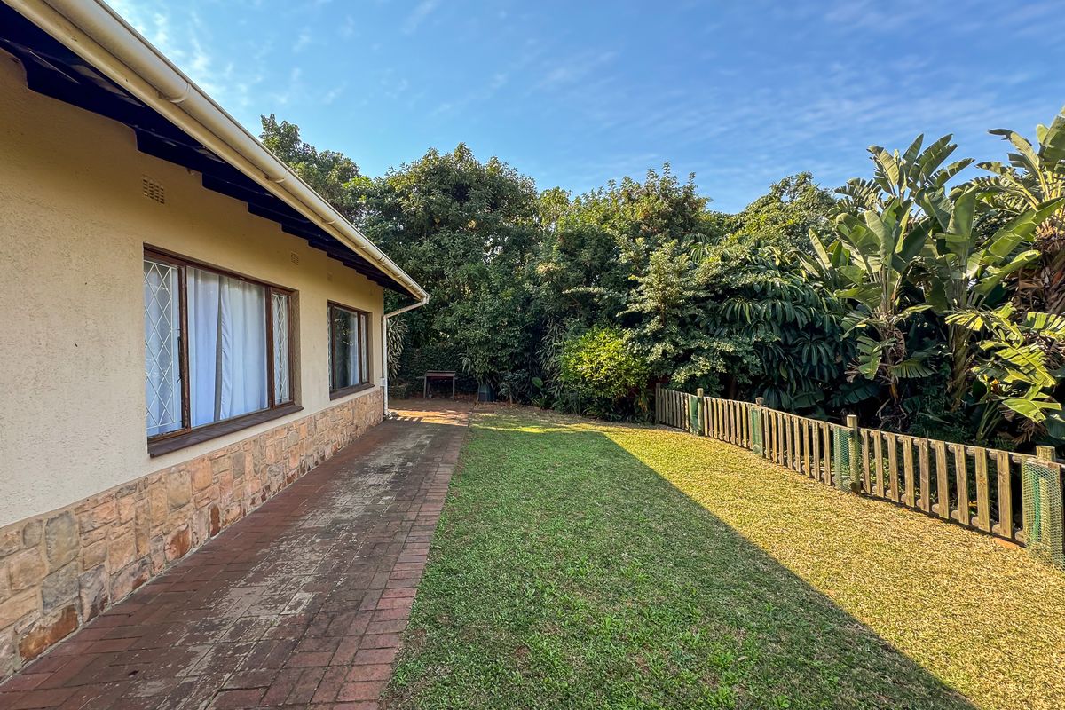 Rear garden area featuring a brick paved walkway, stone-clad exterior wall, and a timber fence bordering the lawn.