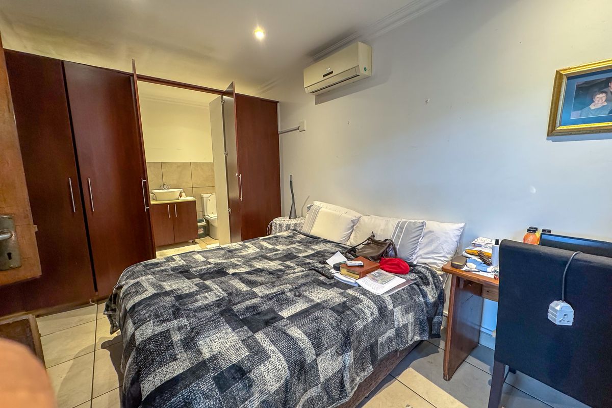 Bedroom featuring built-in cupboards, tiled flooring, split-system air conditioning, and an adjoining en-suite bathroom.