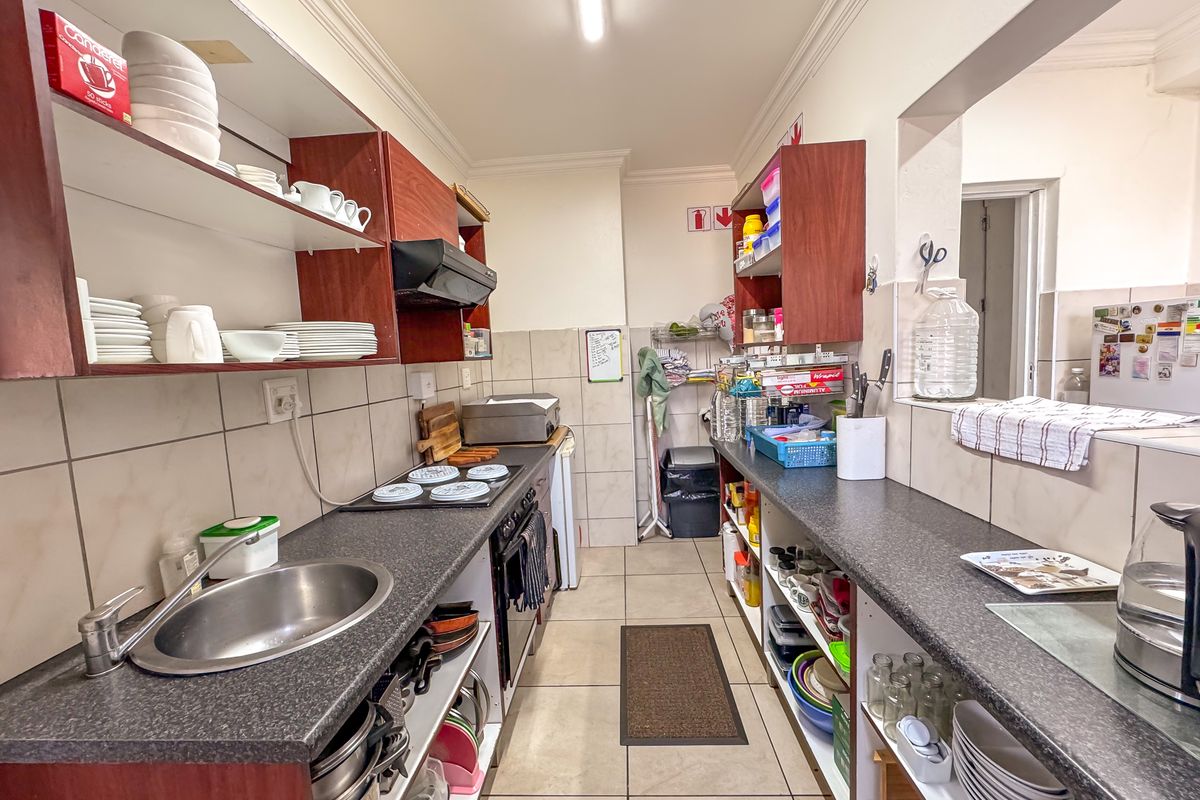 A functional galley-style kitchen featuring built-in cabinetry, laminate countertops, a stainless steel sink, and integrated cooking appliances with tiled finishes throughout.