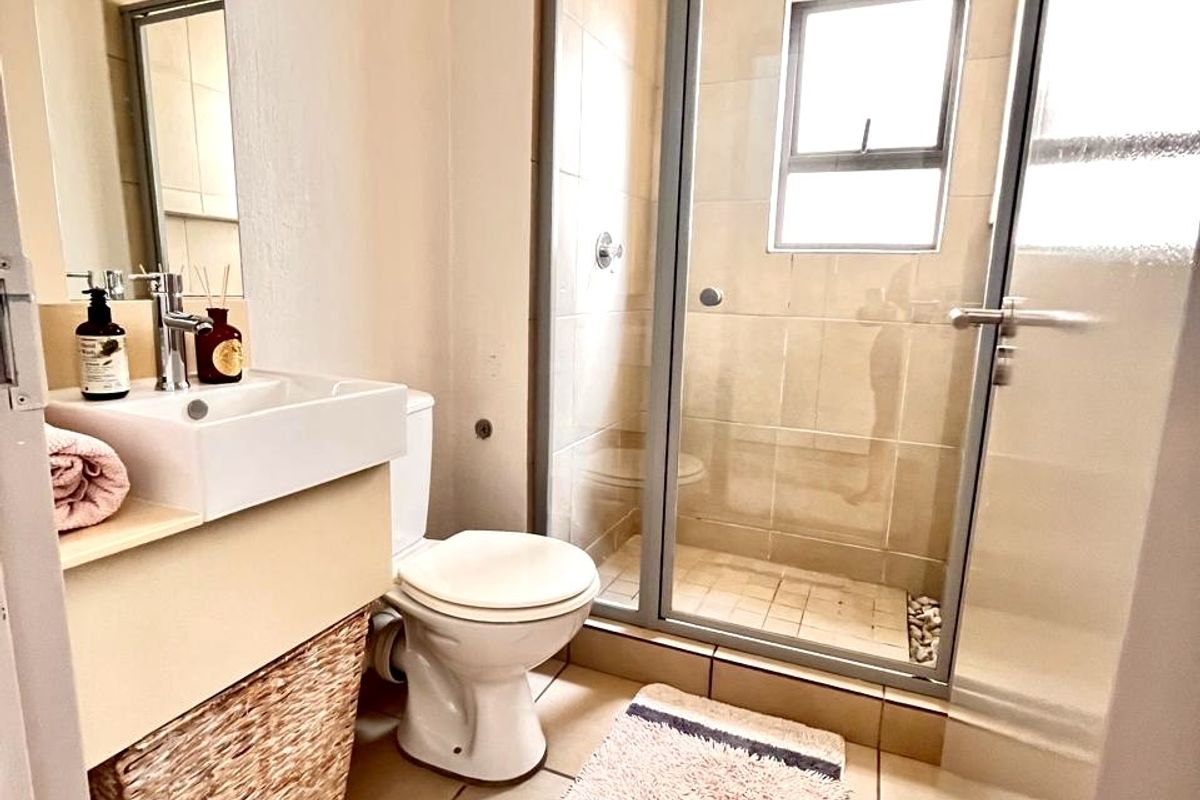 A functional bathroom featuring a shower enclosure, wall-mounted basin, and toilet with neutral floor and wall tiling.