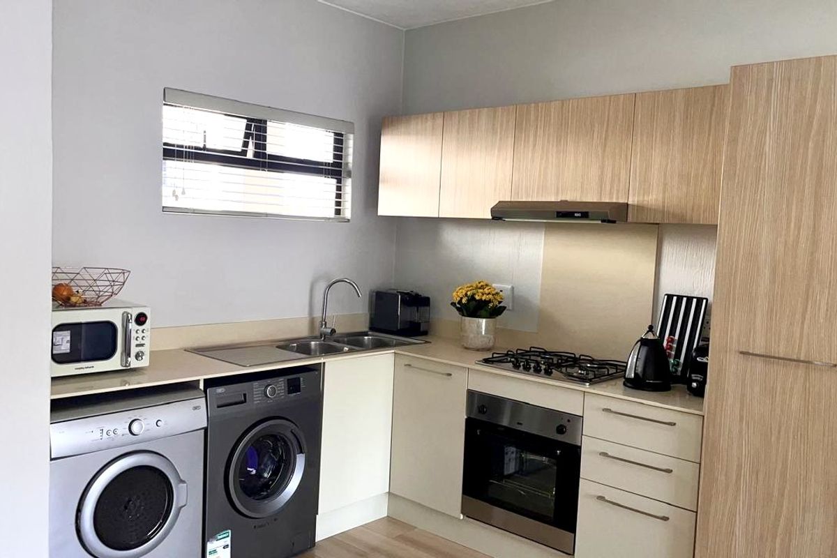 A functional kitchen featuring light wood-finish cabinetry, a gas hob, built-in oven, extractor fan, and integrated space for laundry appliances.
