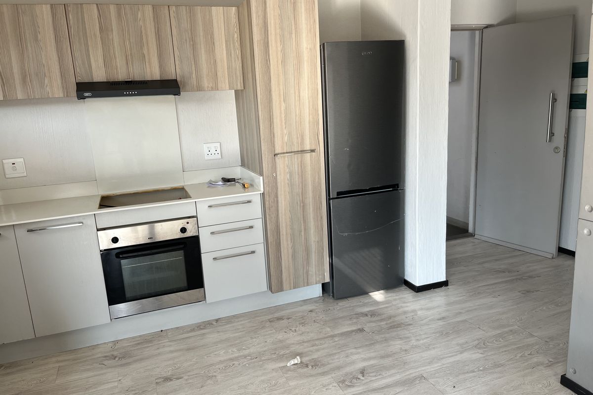 Compact kitchen featuring light wood-grain cabinetry, built-in oven, extractor fan, and laminate flooring, providing a functional space for daily meal preparation.