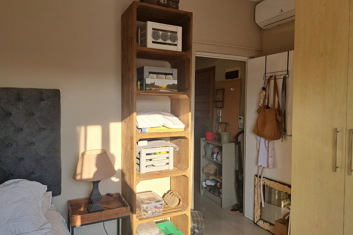 A bedroom featuring a built-in wardrobe, wall-mounted air conditioning unit, and tiled flooring, with an adjacent view into a hallway.