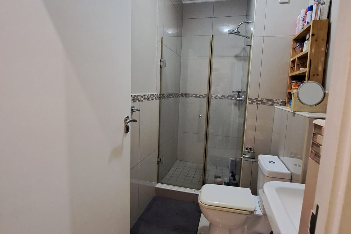 Compact bathroom featuring a glass-enclosed shower, wall-mounted toilet, and pedestal basin with neutral floor-to-ceiling tiling.