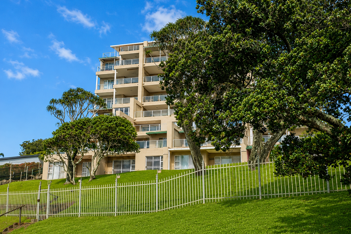 A view of the apartment building exterior featuring multiple levels of balconies and landscaped grounds with a secure perimeter fence.