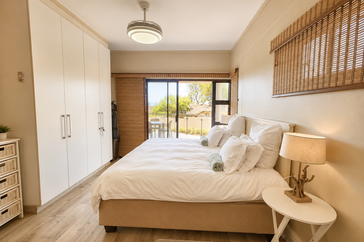 A bright bedroom featuring built-in floor-to-ceiling wardrobes, wood-look flooring, and sliding glass doors leading to a private balcony with scenic views.