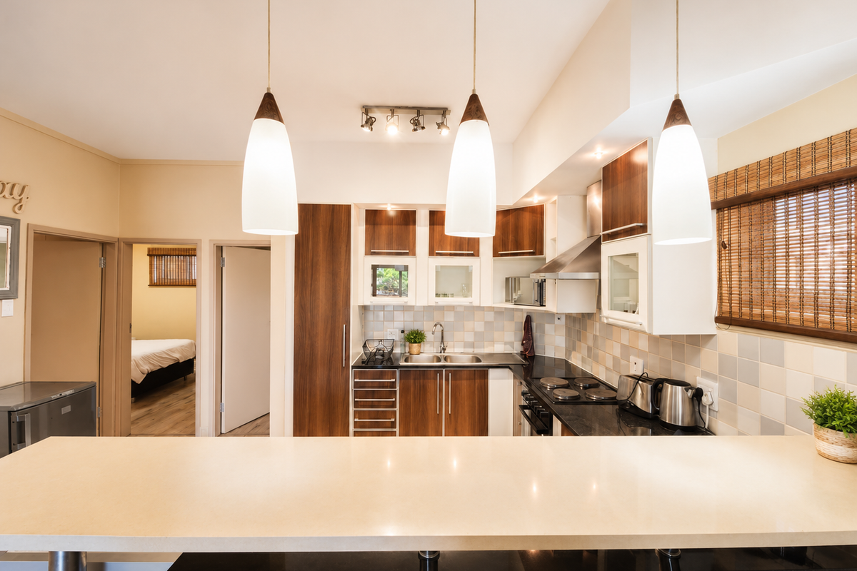 A well-maintained kitchen featuring wood-finish cabinetry, a breakfast bar, integrated hob, extractor fan, and tiled backsplash, opening into a hallway.