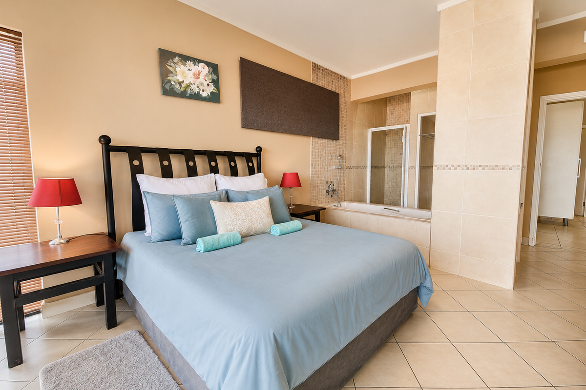 Spacious bedroom featuring an open-plan en-suite bathroom with a built-in bathtub and shower, tiled flooring, and neutral wall finishes.