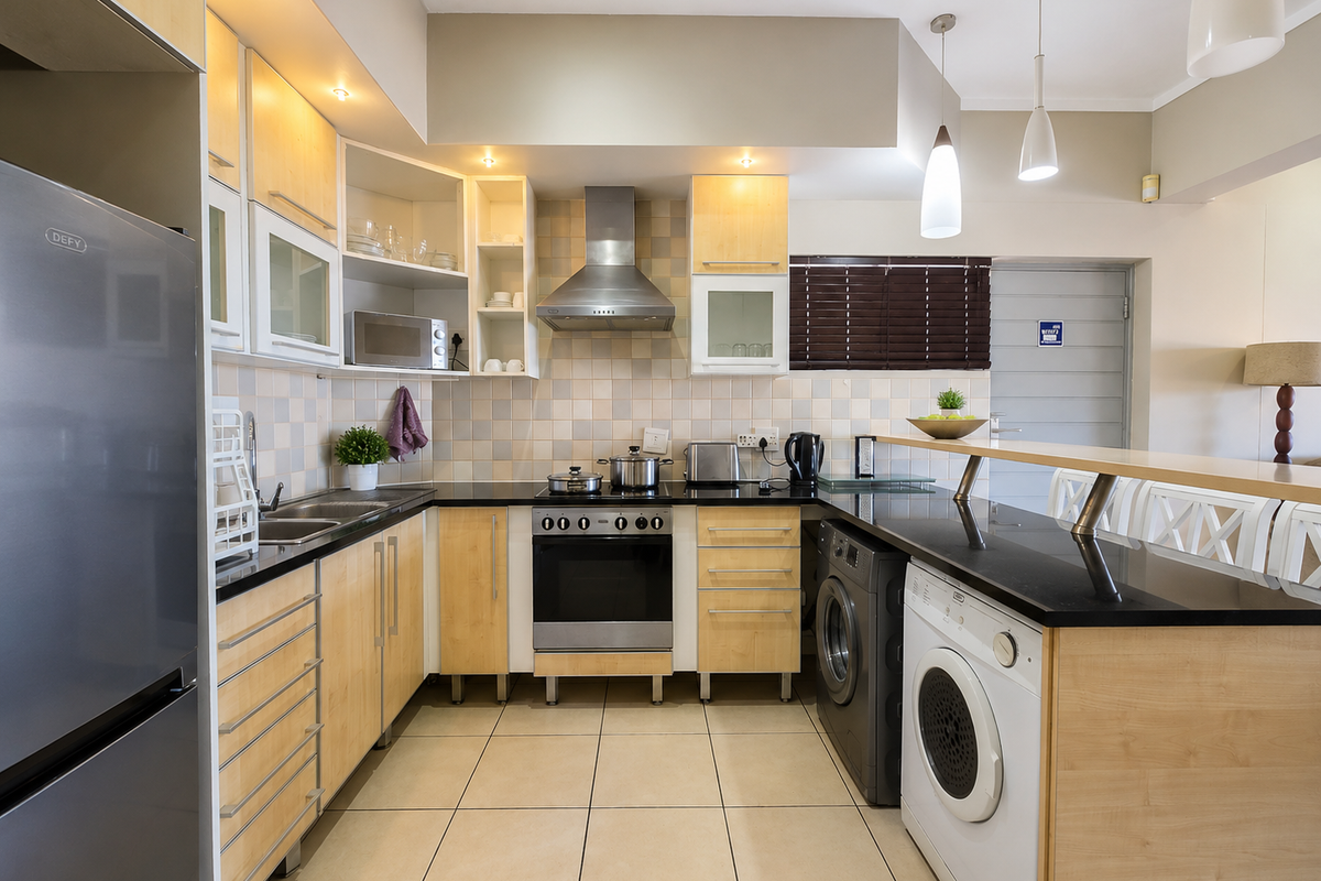 Modern open-plan kitchen featuring light wood cabinetry, black granite countertops, stainless steel extractor fan, built-in oven, and integrated laundry appliances.
