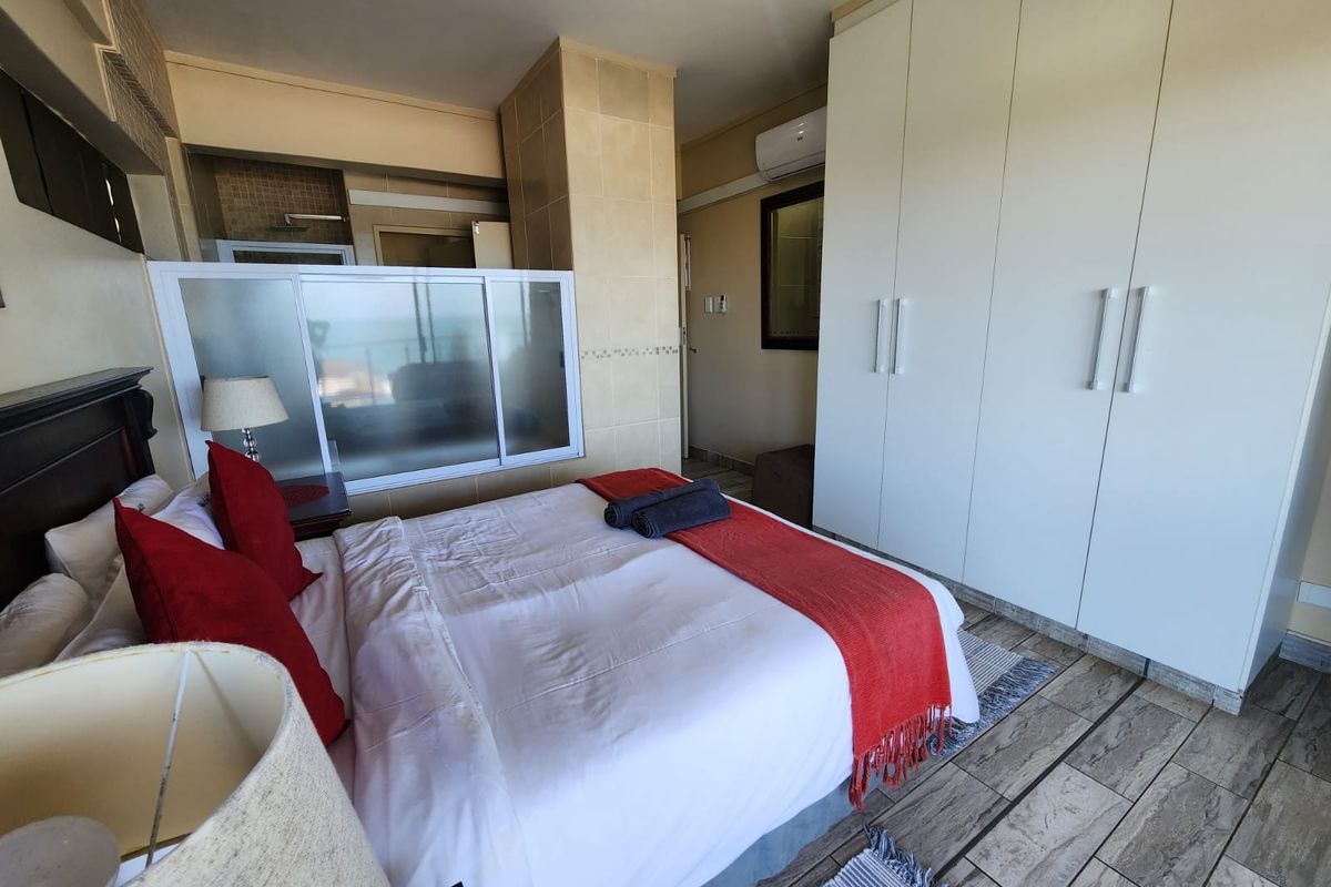 A well-maintained bedroom featuring built-in floor-to-ceiling wardrobes, tiled flooring, and an integrated en-suite bathroom area with a glass partition.