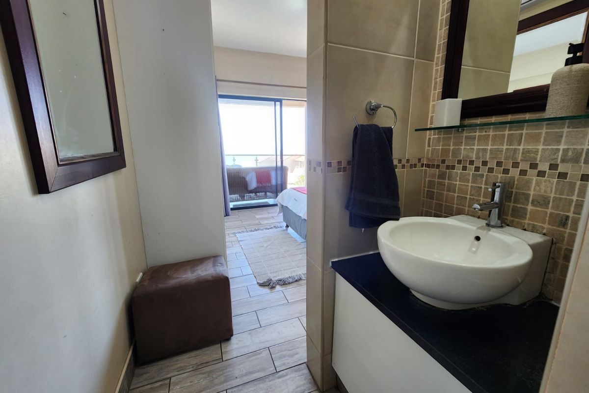 A bathroom vanity area featuring a vessel sink, dark countertop, and mosaic tile backsplash, with a view through to the adjacent bedroom and balcony.