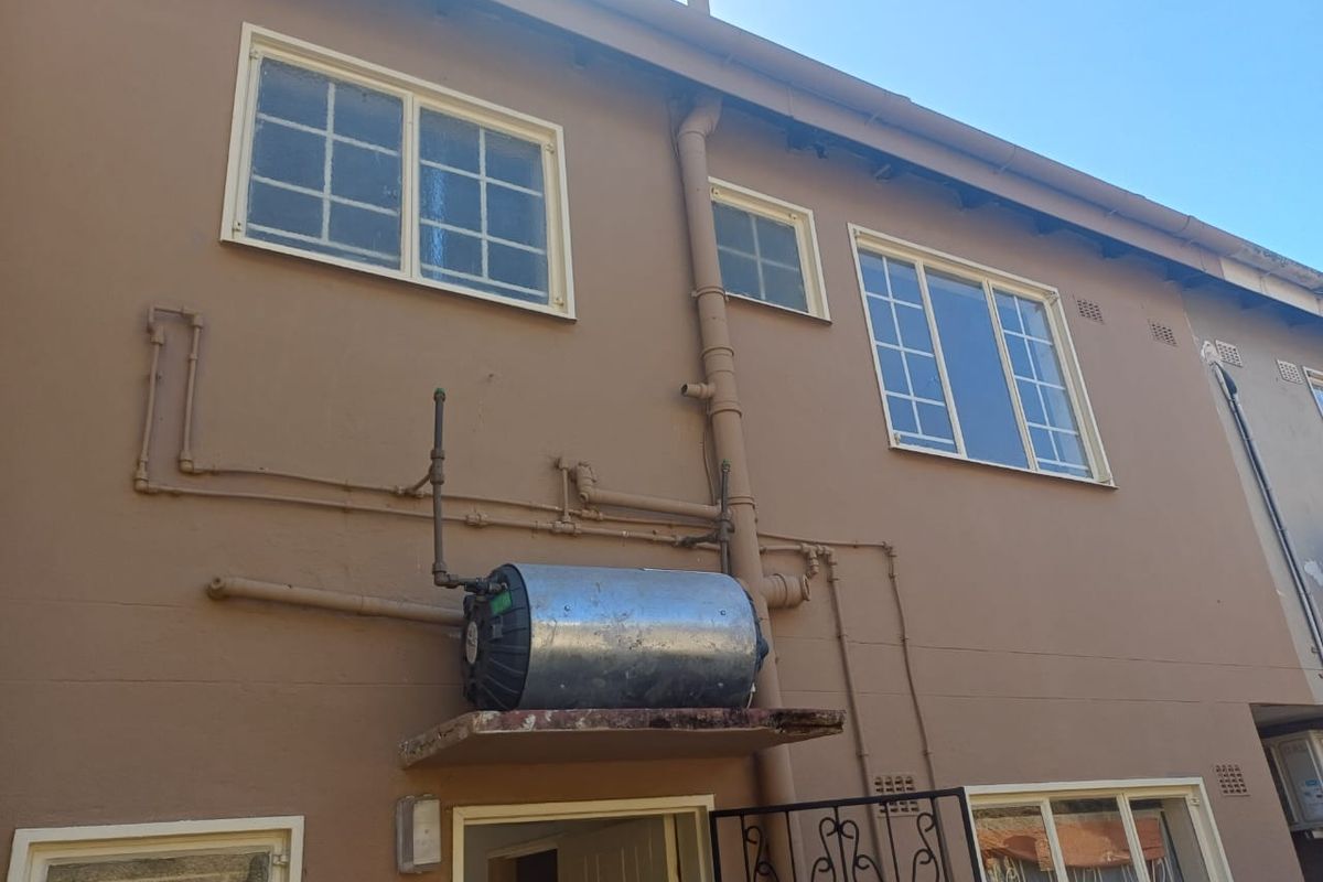 Exterior view of the building facade featuring an externally mounted water heater, exposed plumbing pipes, and multi-pane windows.