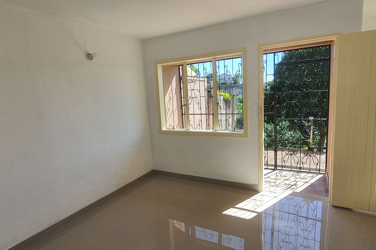 A bright, empty bedroom featuring tiled flooring, security gates on the windows and door, and neutral wall finishes.