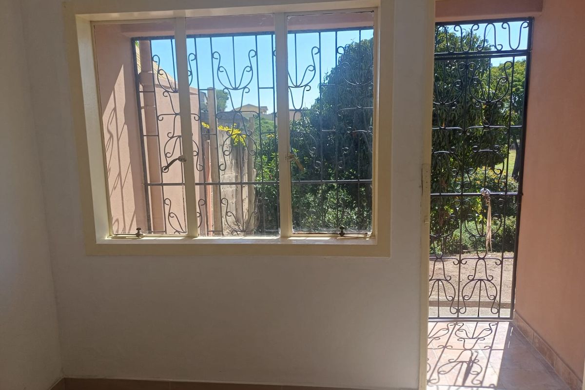 Interior view of a room featuring a large window and a security gate leading to the exterior, providing natural light and garden views.