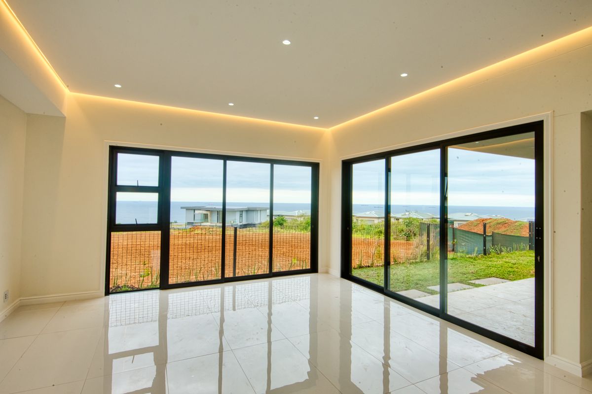 Bright and modern living area featuring large sliding glass doors, polished porcelain tiles, and elegant recessed cove lighting with expansive coastal views.
