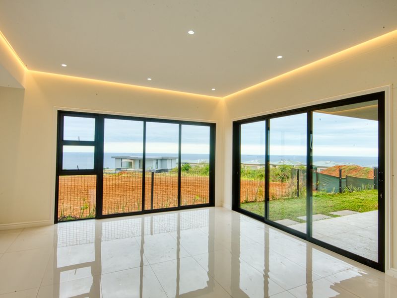 Bright and modern living area featuring large sliding glass doors, polished porcelain tiles, and elegant recessed cove lighting with expansive coastal views.