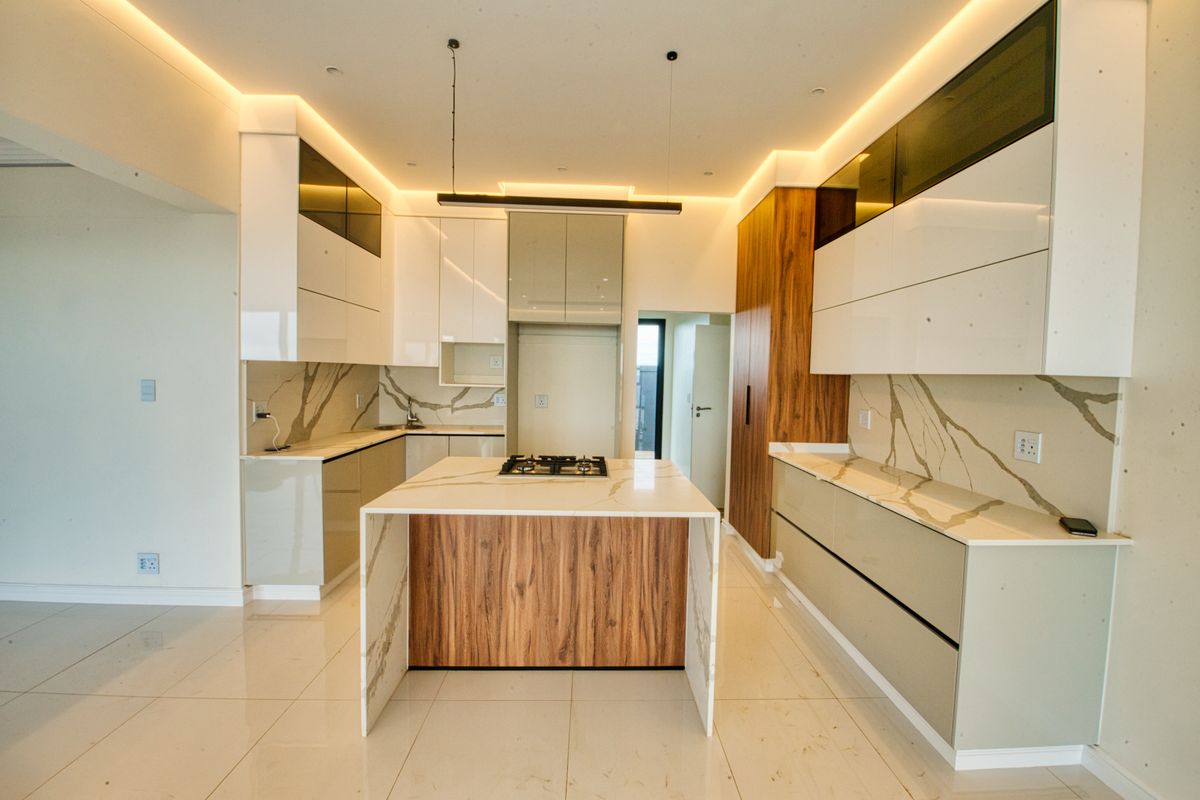 Modern, high-end kitchen featuring a central island with a gas hob, stone countertops, marble-effect splashbacks, and sleek, integrated cabinetry with ambient recessed lighting.
