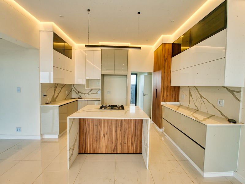 Modern, high-end kitchen featuring a central island with a gas hob, stone countertops, marble-effect splashbacks, and sleek, integrated cabinetry with ambient recessed lighting.