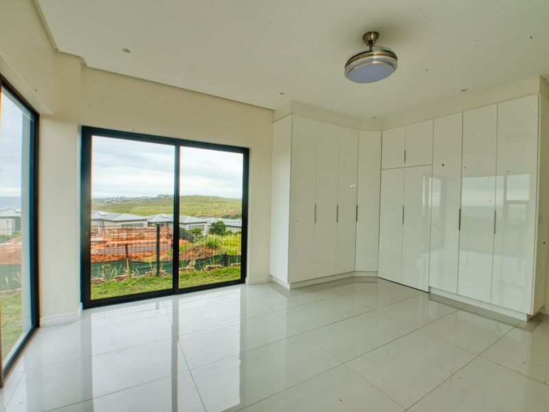 A bright, modern bedroom featuring high-gloss built-in cupboards, large sliding glass doors with scenic views, and polished tiled flooring.