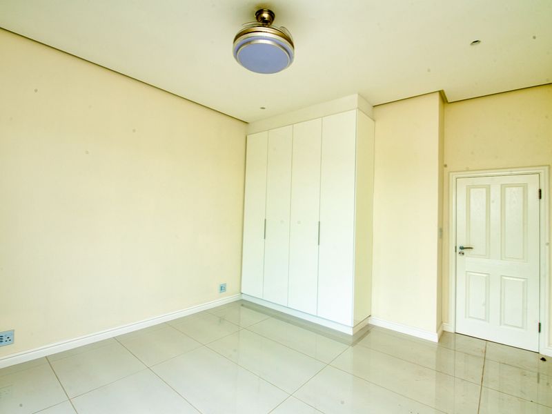 A clean, empty bedroom featuring neutral tiled flooring, a built-in wardrobe, and a ceiling fan, offering a blank canvas for personalization.