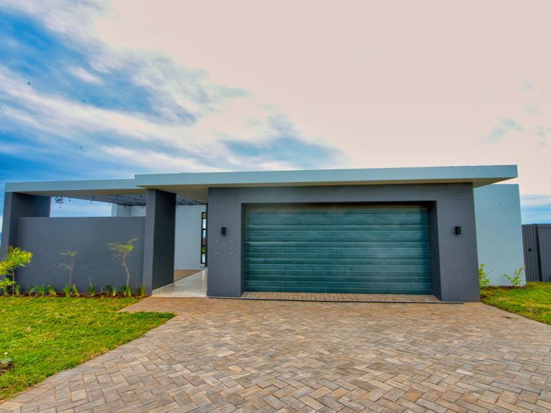 Modern front elevation featuring a paved driveway, automated garage door, and clean architectural lines with integrated outdoor lighting.
