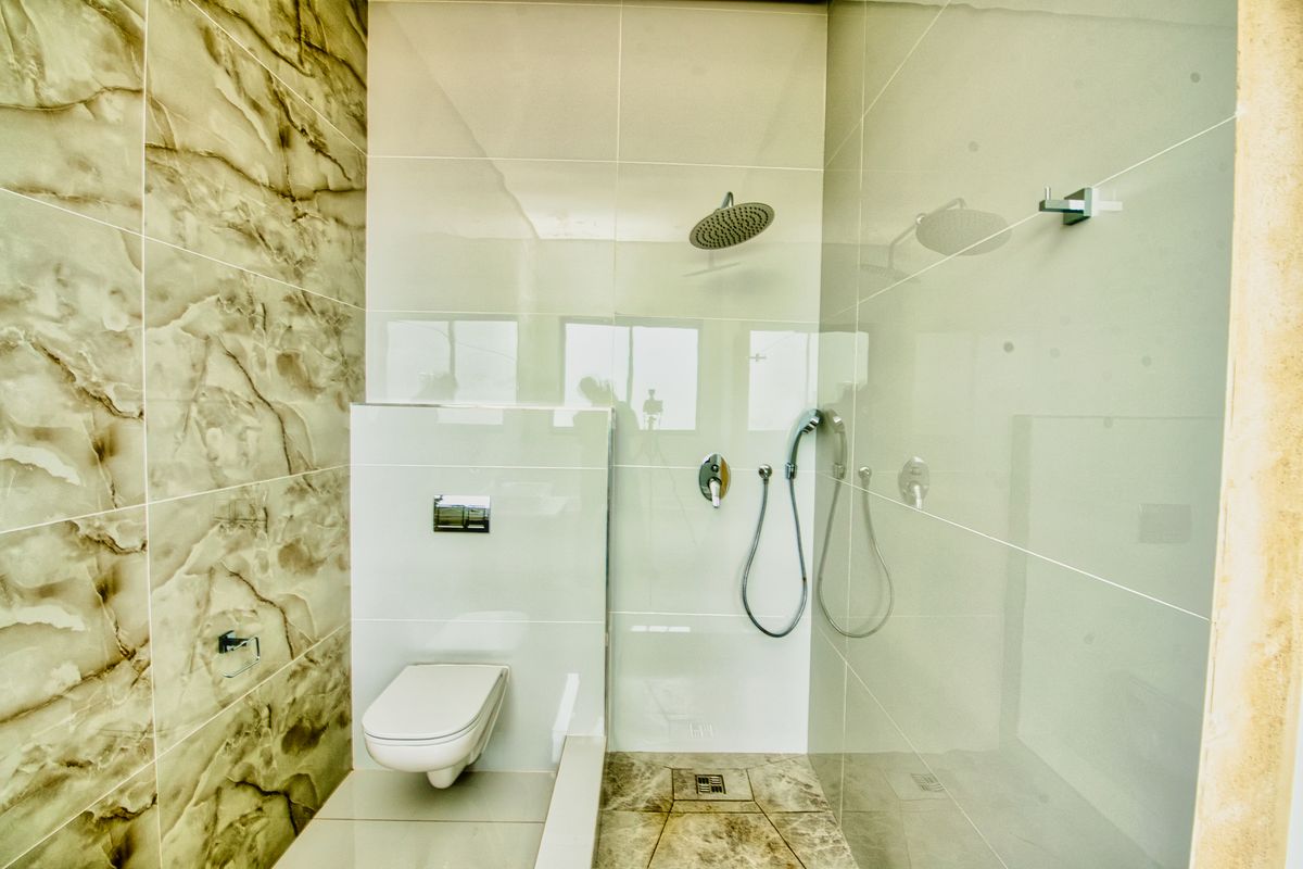 Modern bathroom featuring a wall-mounted toilet with concealed cistern and a walk-in shower area with rain shower head and marble-effect tiling.