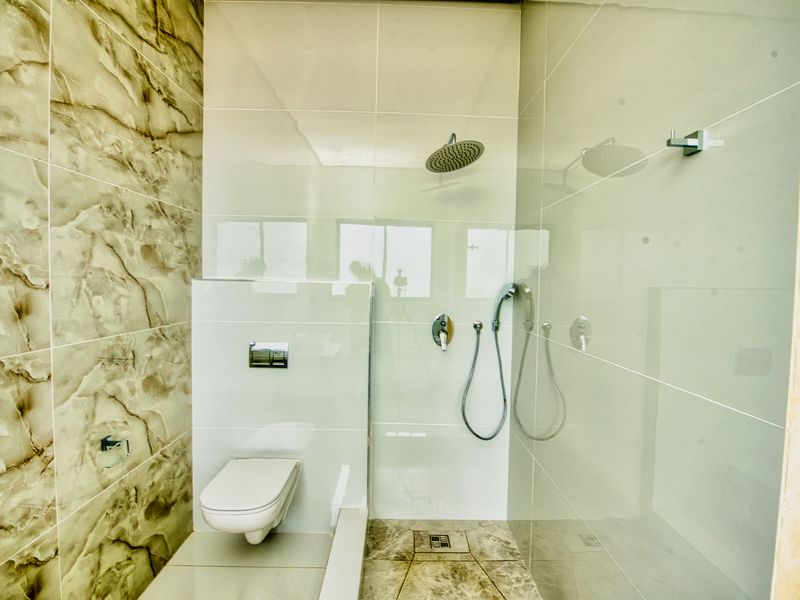 Modern bathroom featuring a wall-mounted toilet with concealed cistern and a walk-in shower area with rain shower head and marble-effect tiling.