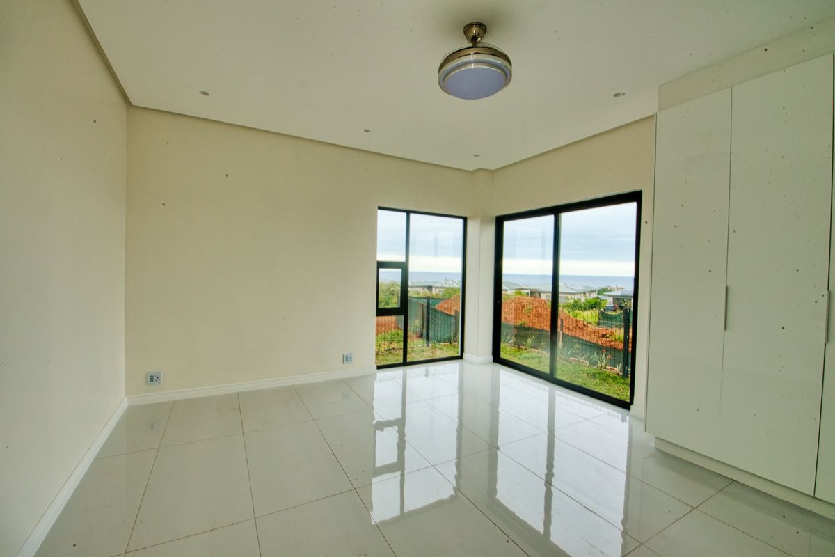 A bright, empty bedroom featuring large sliding glass doors with garden views, tiled flooring, and built-in cupboards.