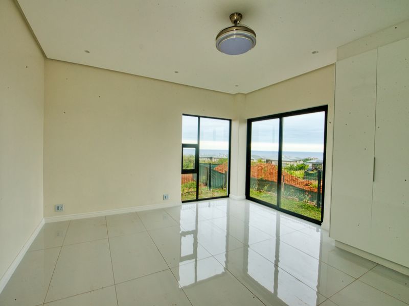 A bright, empty bedroom featuring large sliding glass doors with garden views, tiled flooring, and built-in cupboards.