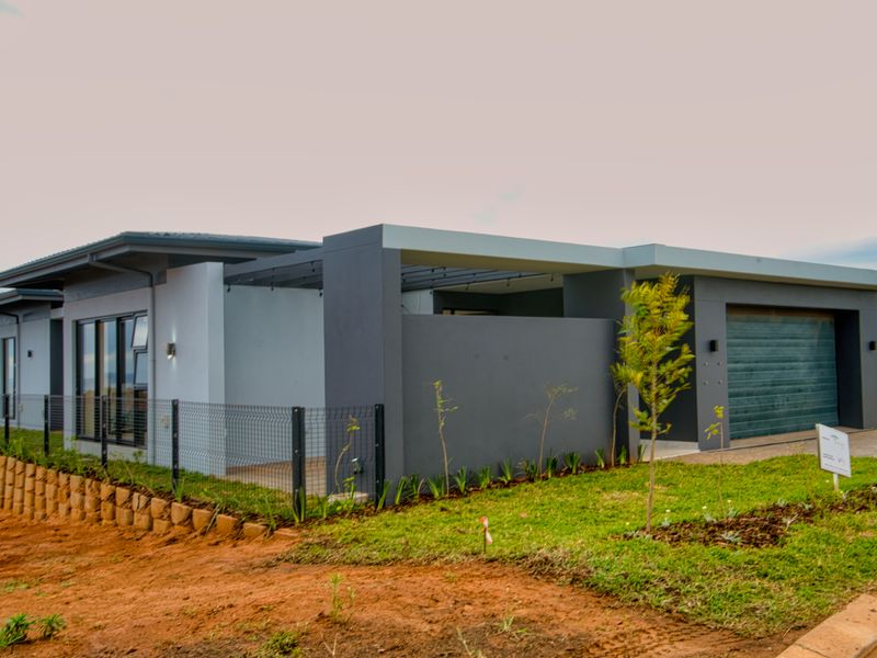 Modern single-story home featuring a double garage, covered patio area, and contemporary grey facade, set on a landscaped plot with retaining walls.