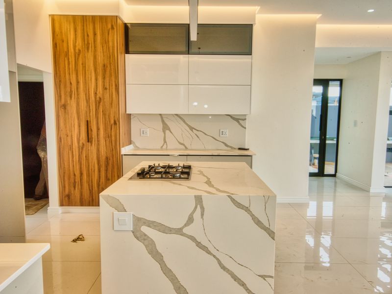 Modern kitchen featuring a central island with a gas hob, stone countertops, and sleek wood-grain and white cabinetry with integrated lighting.