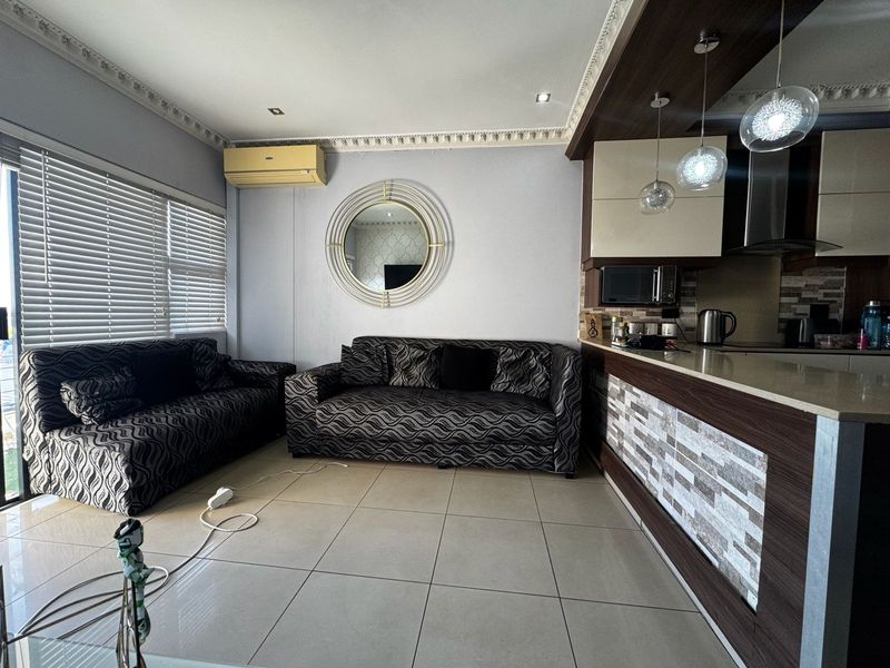 Open-plan living area featuring tiled floors, a modern kitchen with stone countertops, integrated appliances, and decorative ceiling cornices, creating a functional and cohesive space.