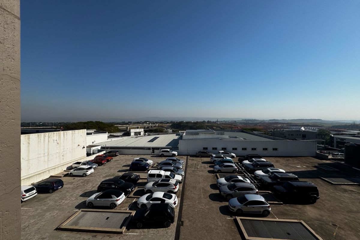 An elevated view of an outdoor parking area with concrete surfacing and surrounding building structures.