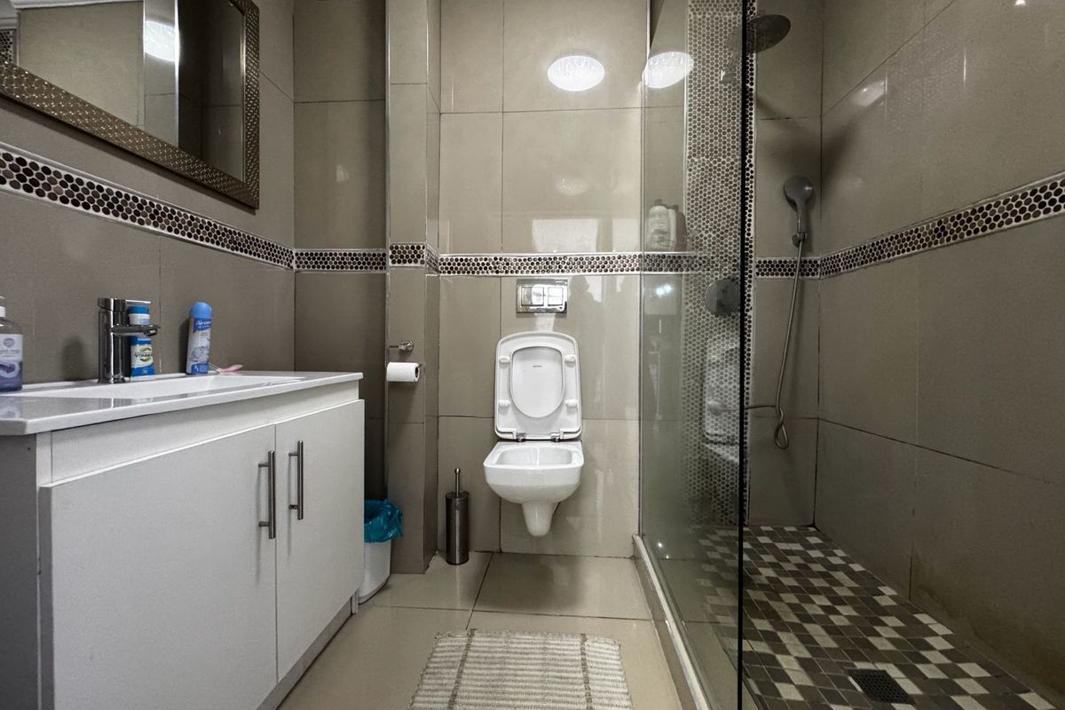 A modern bathroom featuring a wall-mounted toilet, a glass-enclosed shower with a rain shower head, and a vanity cabinet with a basin.