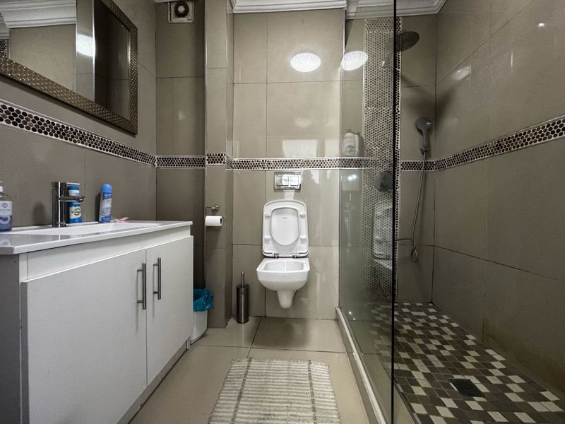 A modern bathroom featuring a wall-mounted toilet, a glass-enclosed shower with a rain shower head, and a vanity cabinet with a basin.