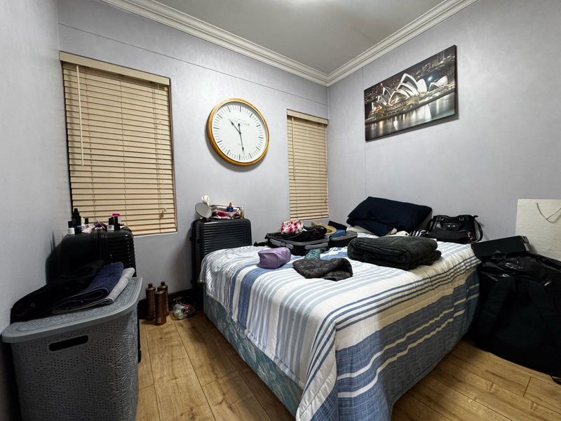 A bedroom featuring laminate flooring, crown molding, and dual windows fitted with venetian blinds.