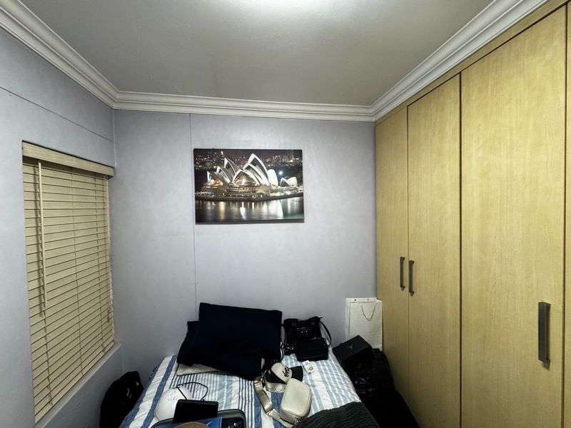 A compact bedroom featuring built-in wooden wardrobes, venetian blinds, and decorative ceiling cornicing.