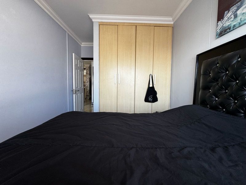 A bedroom featuring light wood-finish built-in wardrobes, decorative ceiling cornices, and a neutral wall palette.