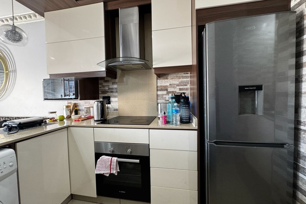 Modern kitchen featuring high-gloss cabinetry, stone countertops, a tiled backsplash, and integrated stainless steel appliances including an oven and extractor fan.