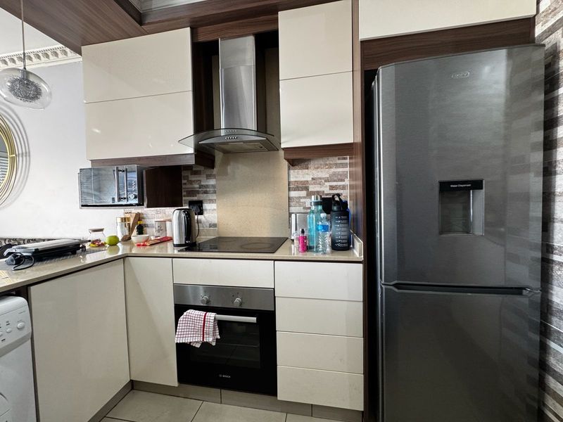 Modern kitchen featuring high-gloss cabinetry, stone countertops, a tiled backsplash, and integrated stainless steel appliances including an oven and extractor fan.