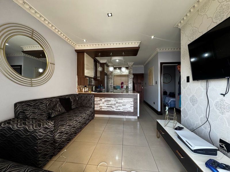 Open-plan living area featuring a modern kitchen with a breakfast bar, tiled flooring, and decorative ceiling cornices, creating a cohesive and functional living space.