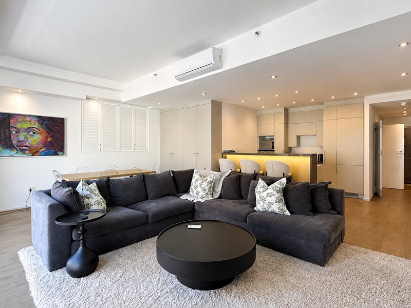 Modern open-plan living area featuring a sleek kitchen with integrated appliances, breakfast bar, recessed lighting, and neutral finishes throughout.